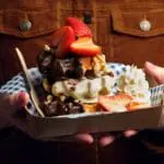 A person holding a tray of waffles topped with strawberries, whipped cream, and a bag of Dr Oetker Professional Dark Chocolate Chips 50% 750g, all presented in a checkered paper container.