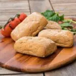 Four bread rolls on wooden board.
