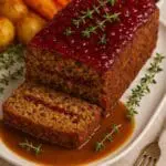 Delicious festive nut roast loaf topped with glossy cranberry sauce and garnished with thyme, served with roast potatoes, carrots, and gravy — a vegan Christmas dinner by Nicol Retailer Limited.