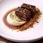 Pressed British diced lamb shoulder served with silky artichoke purée, lemon thyme jus and crispy lamb crumb – recipe and image created by Nicol Retailer