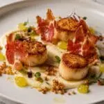 Pan-seared king scallops with crispy Prosciutto Crudo, cauliflower purée, apple gel and hazelnut crumb, beautifully plated in a Michelin-style presentation by Nicol Retailer Limited.