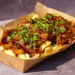 Poutine with fries, cheese curds, Essential Cuisine No1 Beef Gravy 1.5kg, and topped with chopped parsley in a paper tray.
