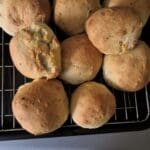 Freshly baked McDougalls' Soft Bap Bread Mix rolls cooling on a wire rack, some with visible herbs.