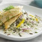 Grilled fish fillet atop a bed of Tilda Easy Cook Basmati & Wild Rice 4kg garnished with dill and slices of yellow bell pepper, served on a white plate.