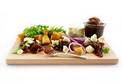 A wooden serving board containing a variety of appetizers including meats, cheeses, and vegetables, accompanied by a side of Arran Fine Foods Caramelised Onion Chutney 2.35kg.