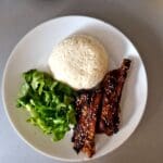 A plate with a scoop of sticky coconut rice, grilled ribs, and a side of chopped green lettuce.