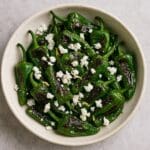 Charred Padron peppers with feta crumble and lemon zest created by Nicol Retailer, served in a rustic ceramic bowl and drizzled with olive oil.