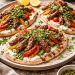 Plated chimichurri beef flatbreads topped with seared British beef stir fry strips, charred peppers, fresh herbs and yoghurt on a rustic ceramic plate