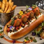 Michelin-Star Mediterranean Falafel Brioche Roll filled with crispy falafel, Provençal ratatouille, whipped vegan feta, roasted red pepper coulis, basil pistou and fresh herbs in a toasted La Boulangerie Vegan Brioche Style Hot Dog Roll.