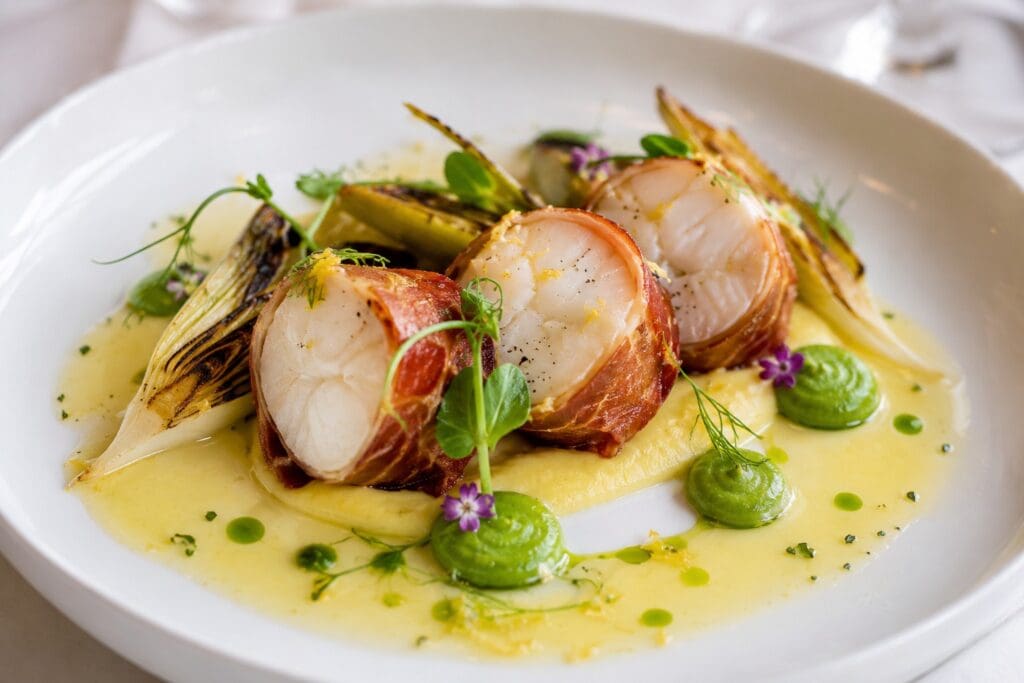 Michelin-inspired San Michele Speck-crusted monkfish with saffron cauliflower velouté, pea purée, charred leeks and Champagne beurre blanc, created by Nicol Retailer Limited